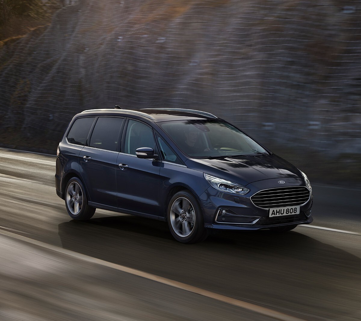 Ford Galaxy Hybrid in Blau. 3/4-Frontansicht. Fahrszene auf einer Bergpanorama-Straße