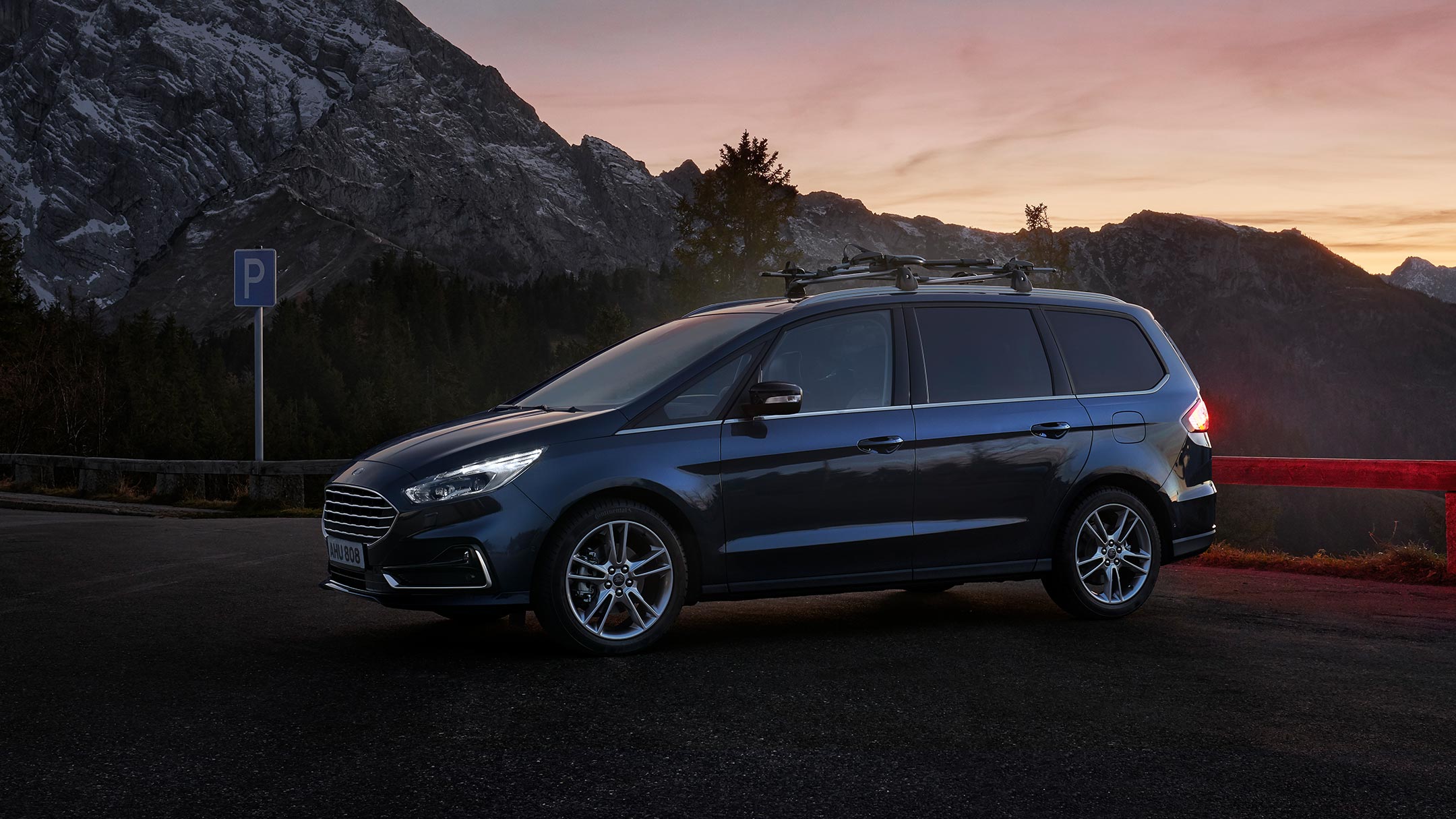 Ford Galaxy Hybrid in Blau. ¾-Frontansicht. Auf Kies vor einem Haus parkend