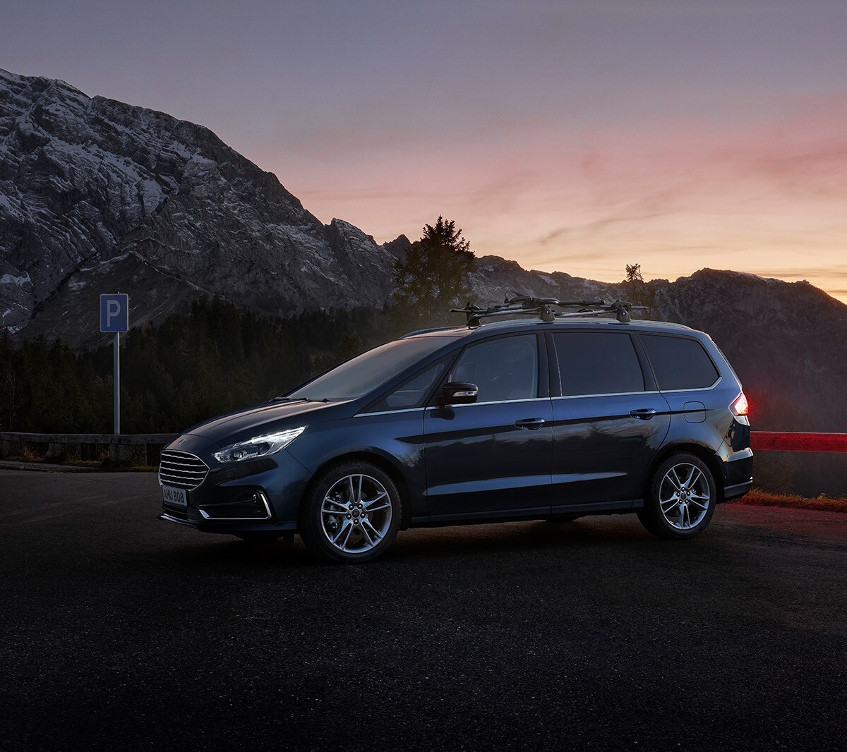 Ford Galaxy Hybrid in Blau. Seitanansicht. Bei untergehender Sonne mit Bergen im Hintergrund parkend
