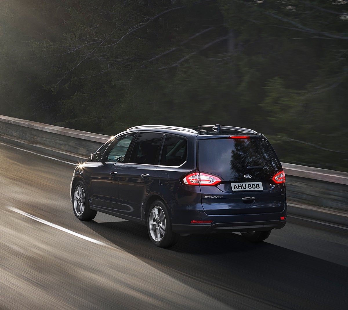Ford Galaxy Hybrid in Grau, Dreiviertelansicht, bei Sonnenschein entlang einer Küstenstraße fahrend