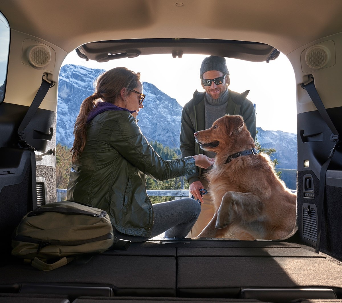 Ford Galaxy Hybrid. Blick von innen durch die geöffnete Heckklappe. Hund und Frau auf der Ladekante sitzend, Mann vor der Heckklappe stehend.