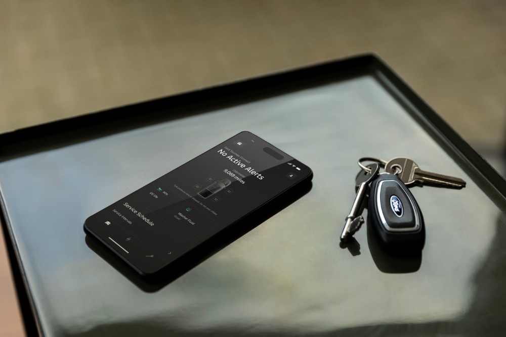 Ein Smartphone zeigt die Ford App mit Fahrzeugstatus neben einem Ford Autoschlüssel.