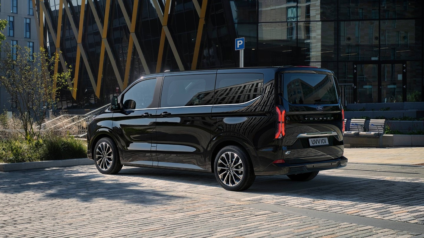 Ford Tourneo Custom in Schwarz in der ¾ Heckansicht geparkt auf einem Parkplatz vor modernen Gebäuden
