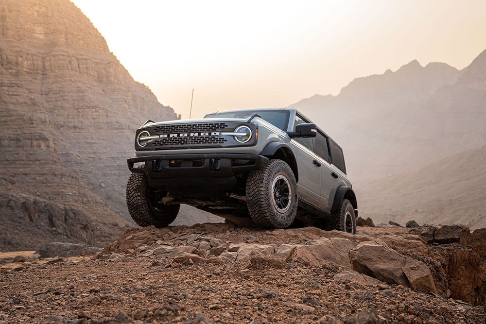 Ein grauer Ford Bronco parkte auf einem felsigen Pfad in einer Bergkulisse.