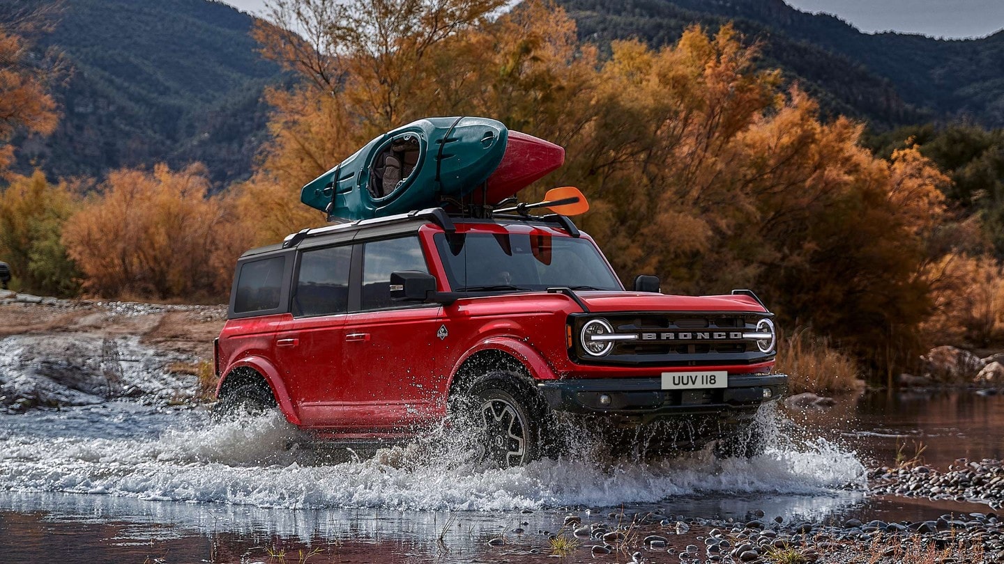 Ford Bronco in Rot. In 3/4-Frontansicht in felsiger Landschaft durch einen Wasserlauf fahrend