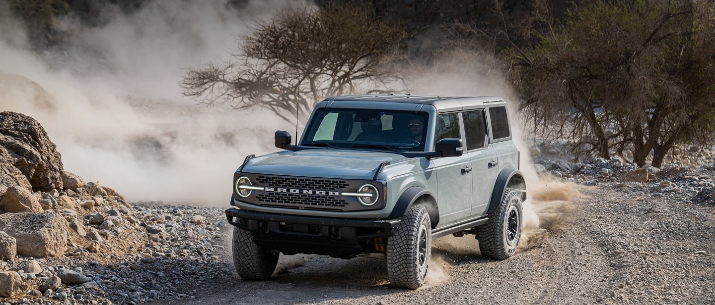 Ford Bronco in Grau, in 3/4-Frontansicht. Auf staubigem Schotterweg um eine Kurve fahrend