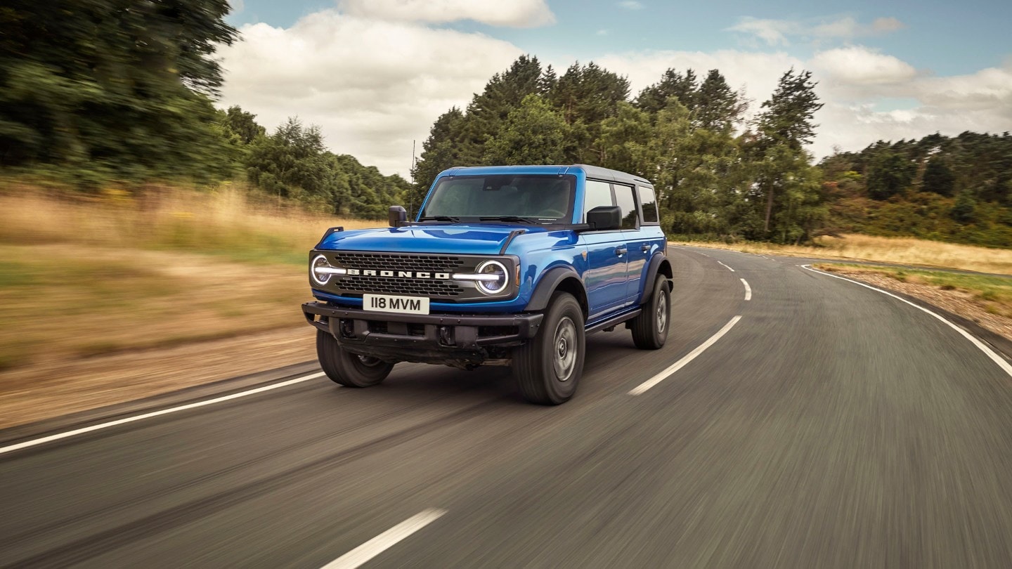 Ford Bronco in Blau in 3/4-Frontansicht auf einer Landstraße fahrend