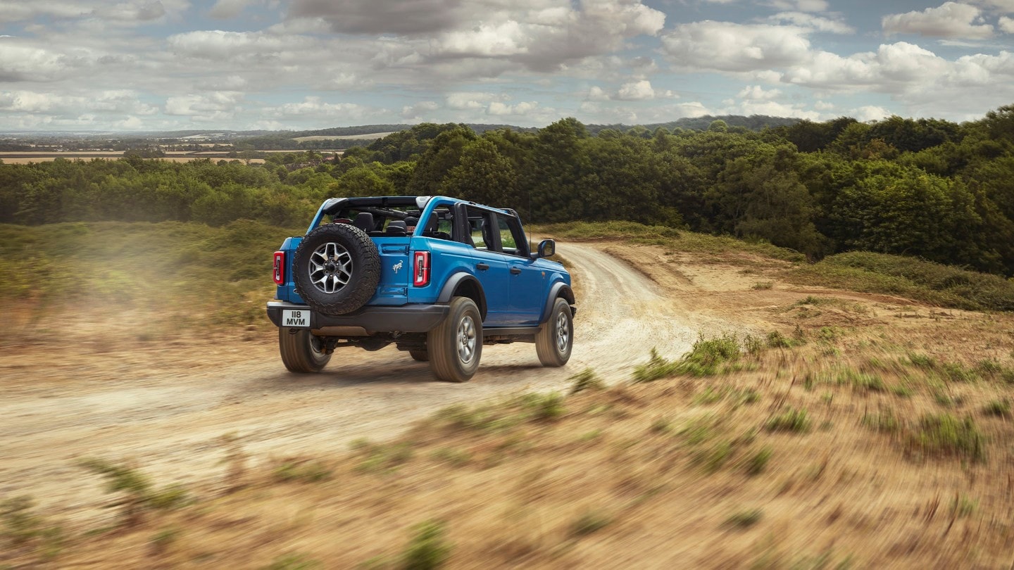 Ford Bronco in Blau, in 3/4-Heckansicht. Auf einem Feldweg fahrend