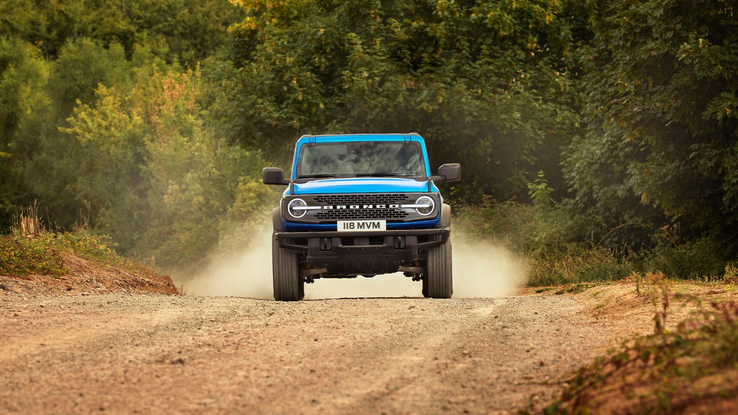 Ford Bronco in Blau, in Frontansicht, auf einem staubigen Weg fahrend