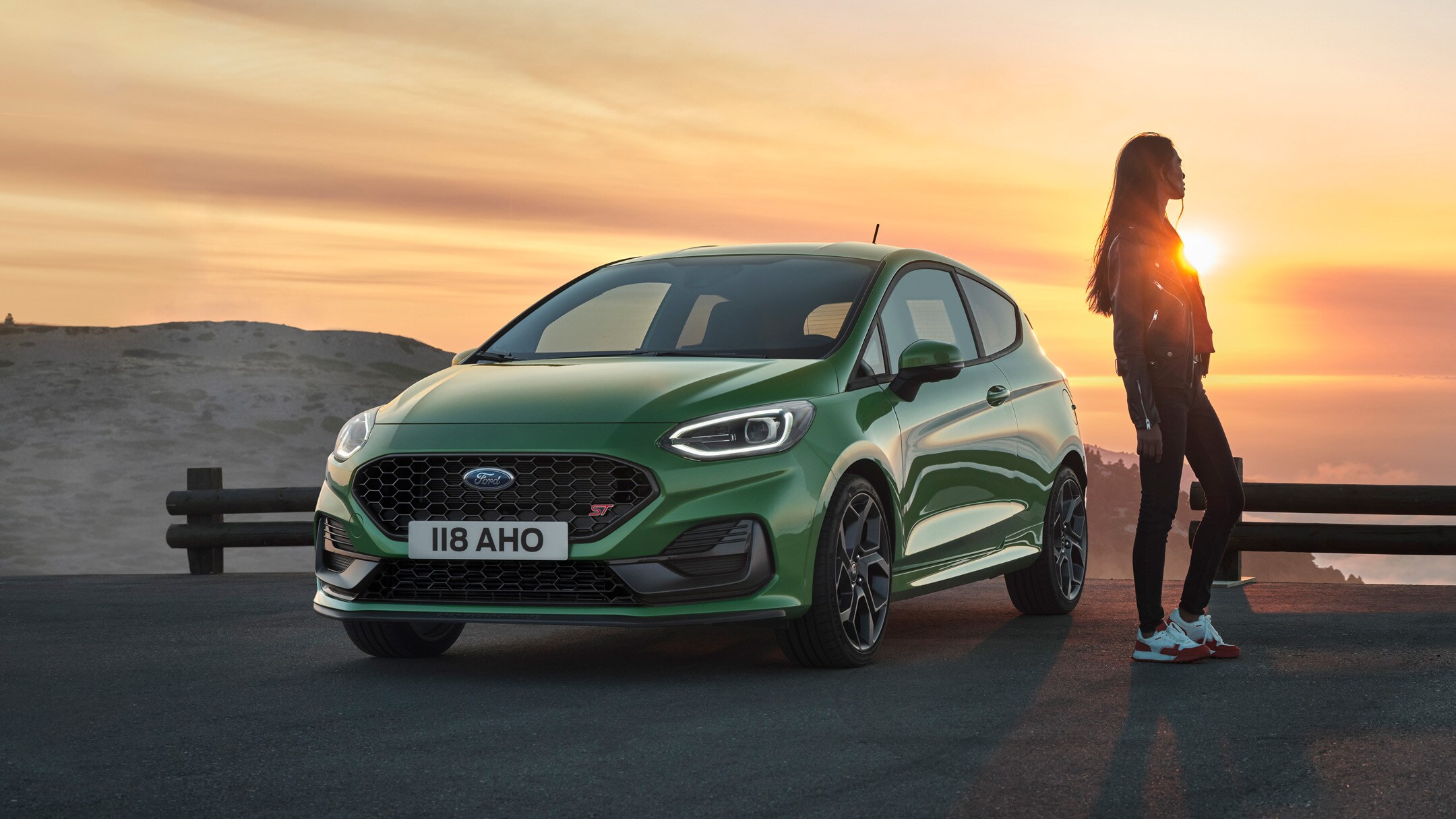 Ford Fiesta ST in Grün in der 3/4 Frontansicht auf einem Parkplatz bei Sonnenuntergang 