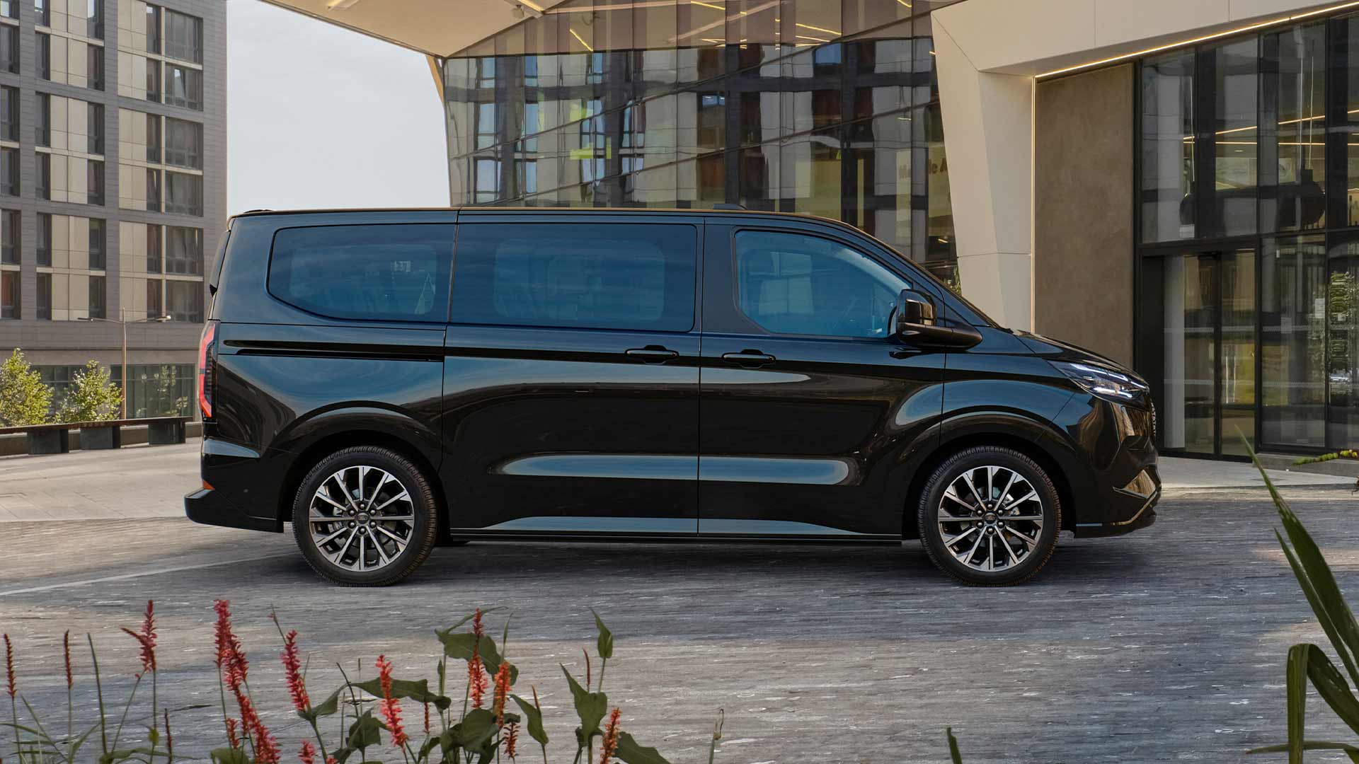 Schwarzer Ford E-Tourneo Custom vor modernem Gebaeude geparkt