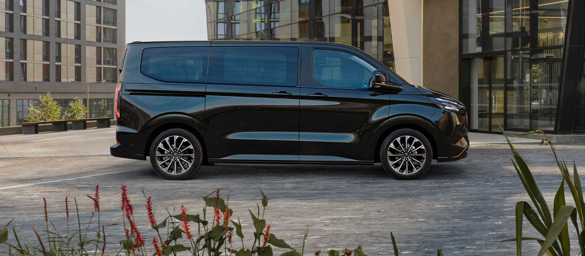 Schwarzer Ford E-Tourneo Custom vor modernem Gebaeude geparkt