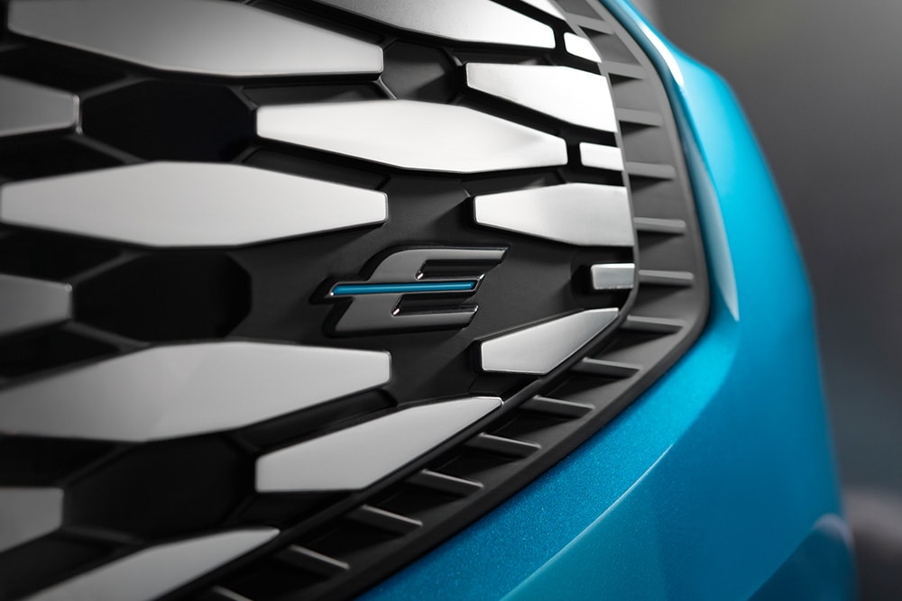 Nahaufnahme des Ford E-Tourneo Custom Kühlergrills mit blauem \E\" Logo, exklusiv fuer Ford Elektrofahrzeuge"