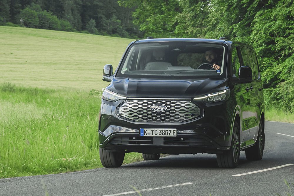 Schwarzer Ford E-Tourneo Custom faehrt auf Landstrasse