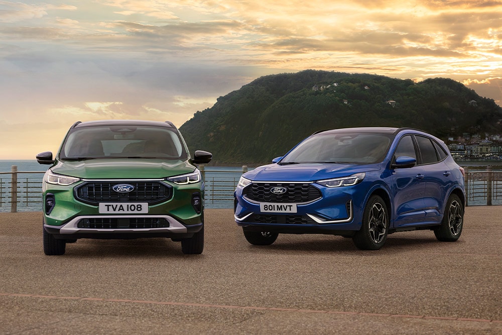 Ein grüner Ford Kuga Active und ein blauer Ford Kuga ST Line Seite an Seite auf einem Küstenparkplatz geparkt. 