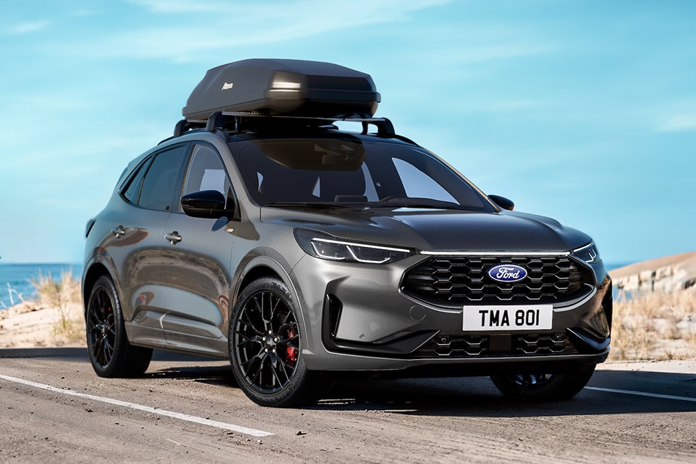 Grauer Ford Kuga mit zwei Mountainbikes auf einem Fahrradträger, geparkt in einer urbanen Umgebung.