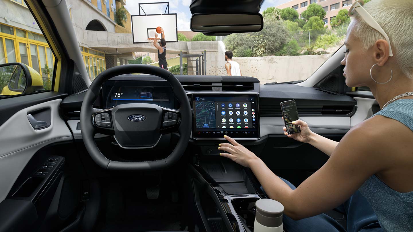 Innenraum des elektrischen Ford Puma Gen-E ®, während eine Person ein Mobiltelefon kabellos mit dem Touchscreen synchronisiert.