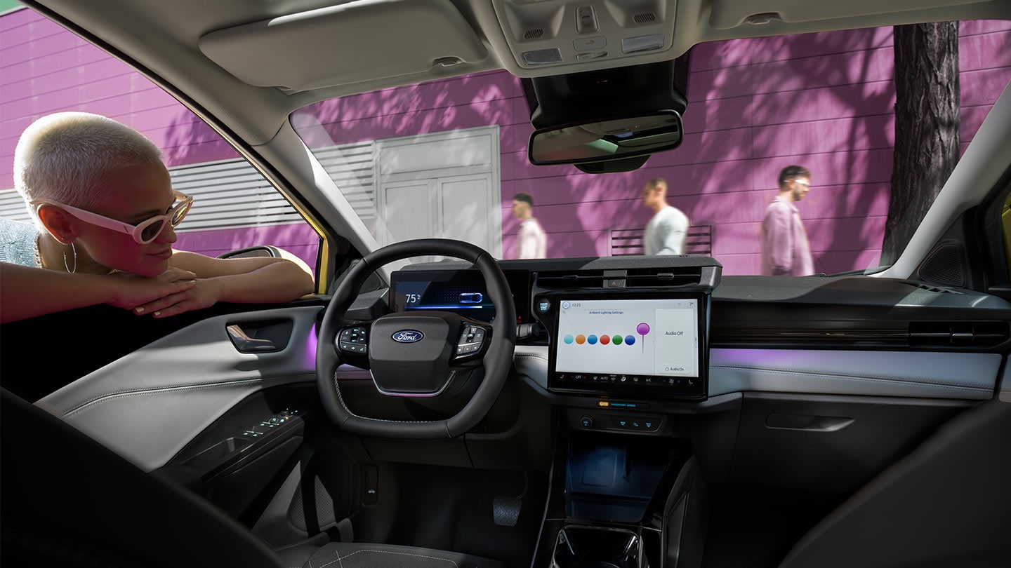 Person, die durch das offene Fenster der Fahrertür in den Innenraum des Ford Puma Gen-E® schaut und sich den großen Touchscreen und die Innenraumbeleuchtung ansieht.