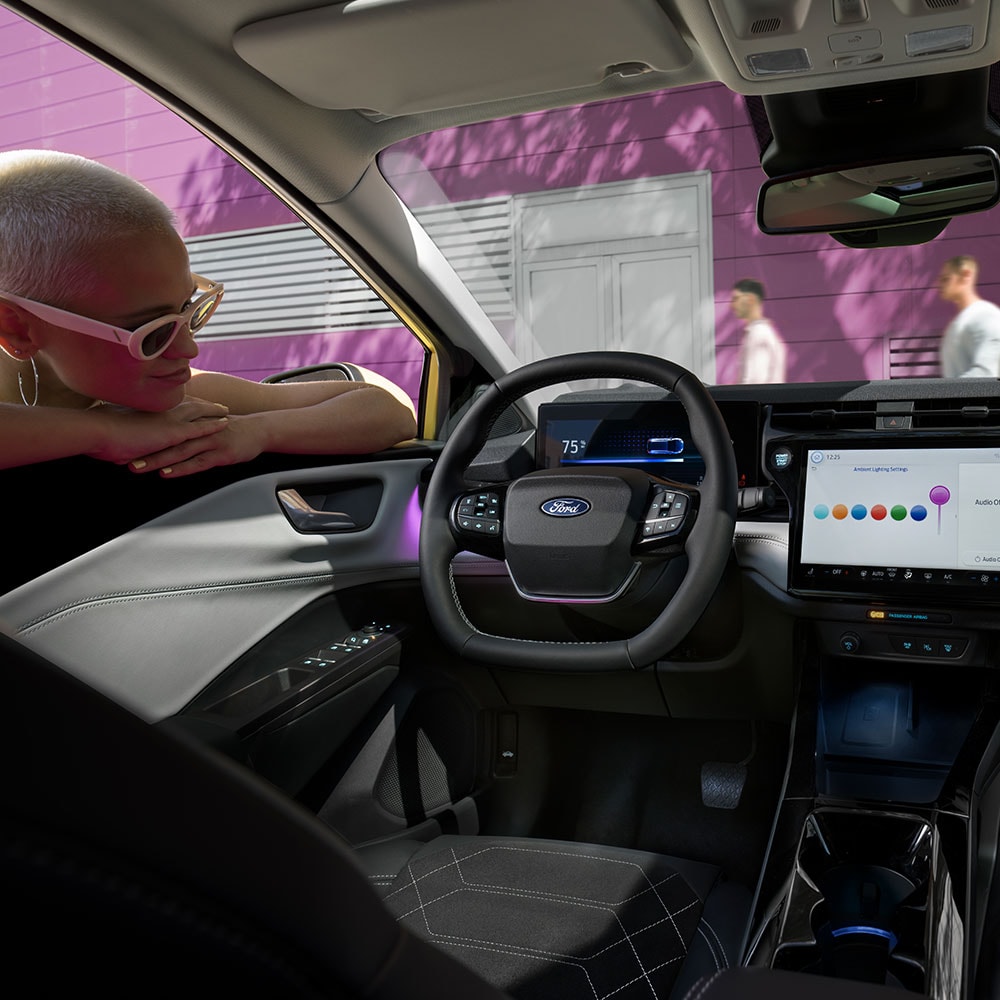 Innenraum des elektrischen Ford Puma Gen-E ®, während eine Person den Infotainment-Bildschirm durch das offener Fenster der Fahrertür betrachtet.