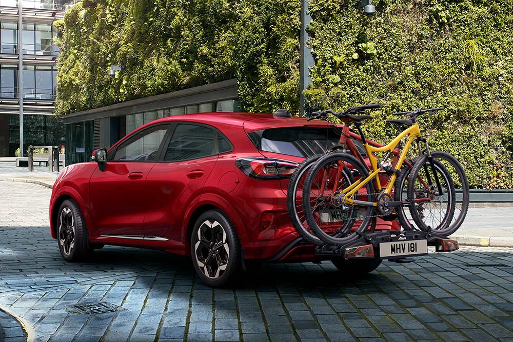 Rot Ford Puma mit zwei Mountainbikes auf einem Fahrradträger, geparkt in einer urbanen Umgebung.