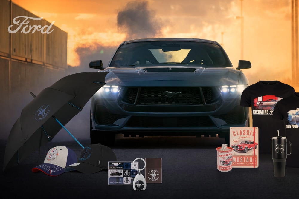 Ford Mustang im Hintergrund mit Mustang-Merchandise: Kleidung, Tassen, Schirme und Sammlerstücke im Vordergrund.