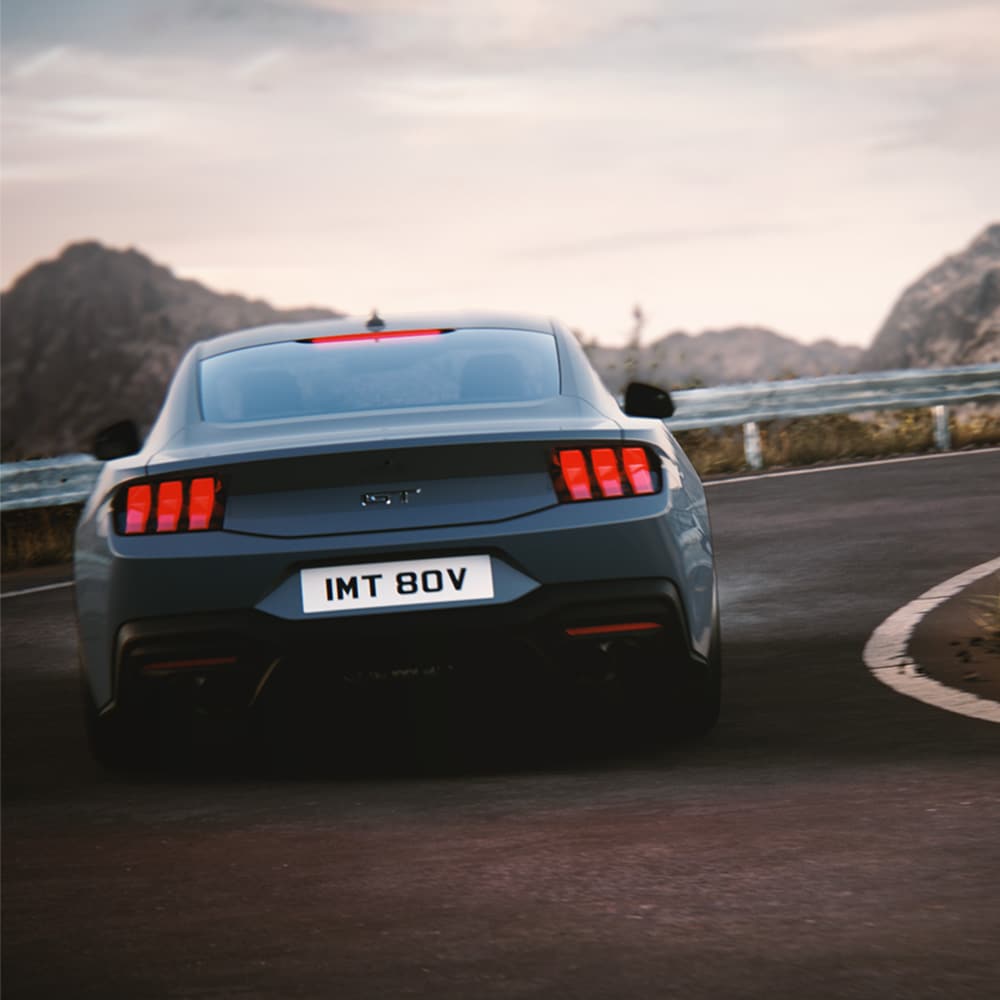 Das Heck eines Ford Mustang GT Fastback in der Farbe blau bei der Fahrt um eine Kurve.