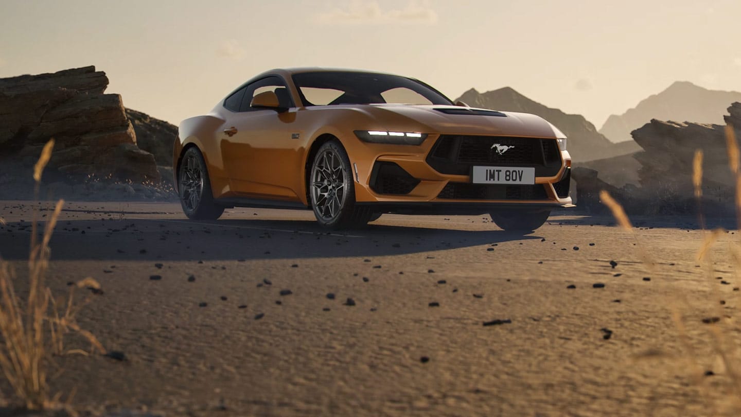 Side view of an orange Ford Mustang parked in a rocky desert landscape.