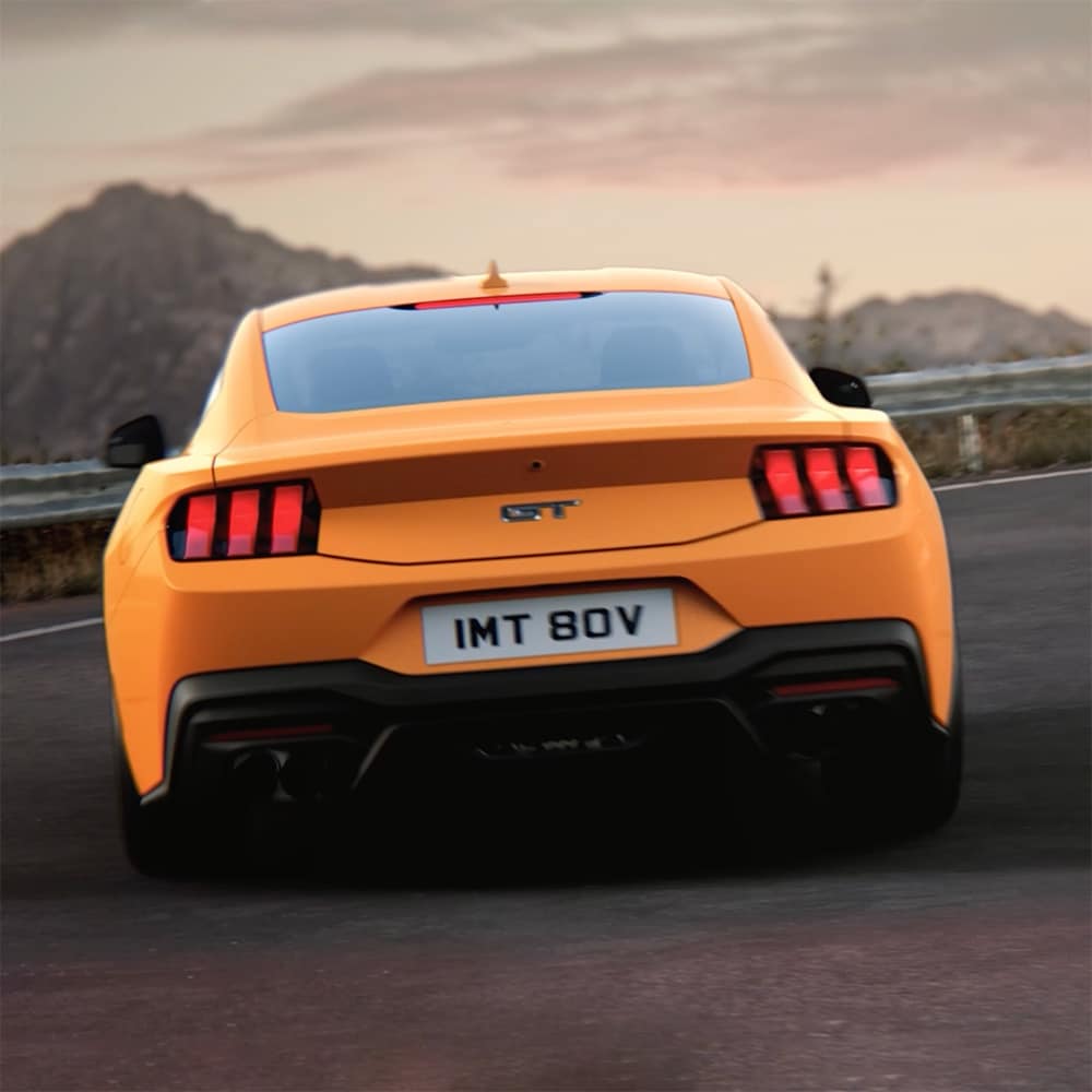 Das Heck eines Ford Mustang GT Fastback in der Farbe blau bei der Fahrt um eine Kurve.