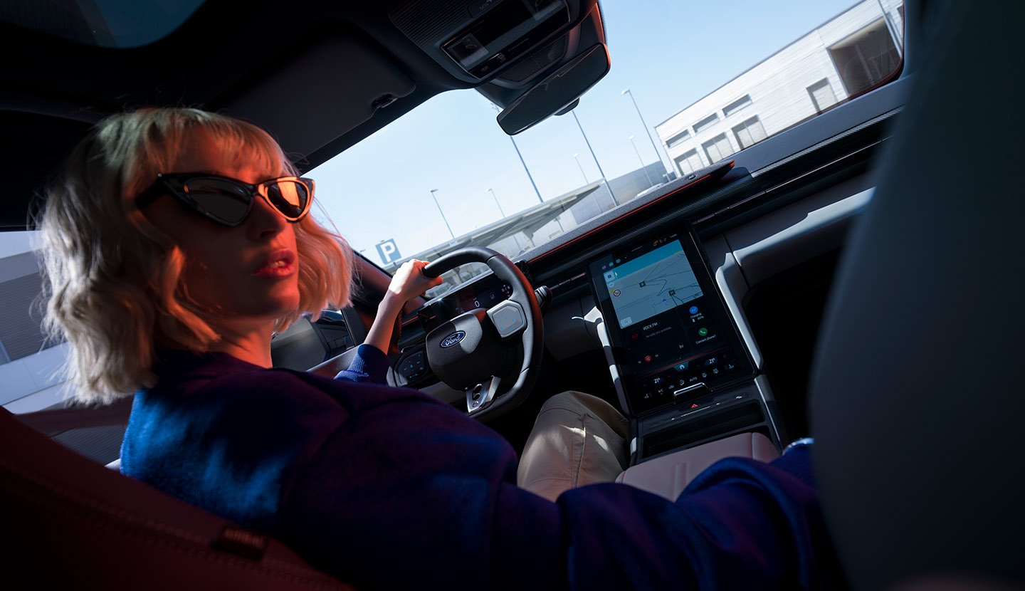 Eine Frau sitzt auf dem Fahrersitz eines geparkten Ford Capri®, wobei das Lenkrad und der große SYNC® Move-Touchscreen sichtbar sind.