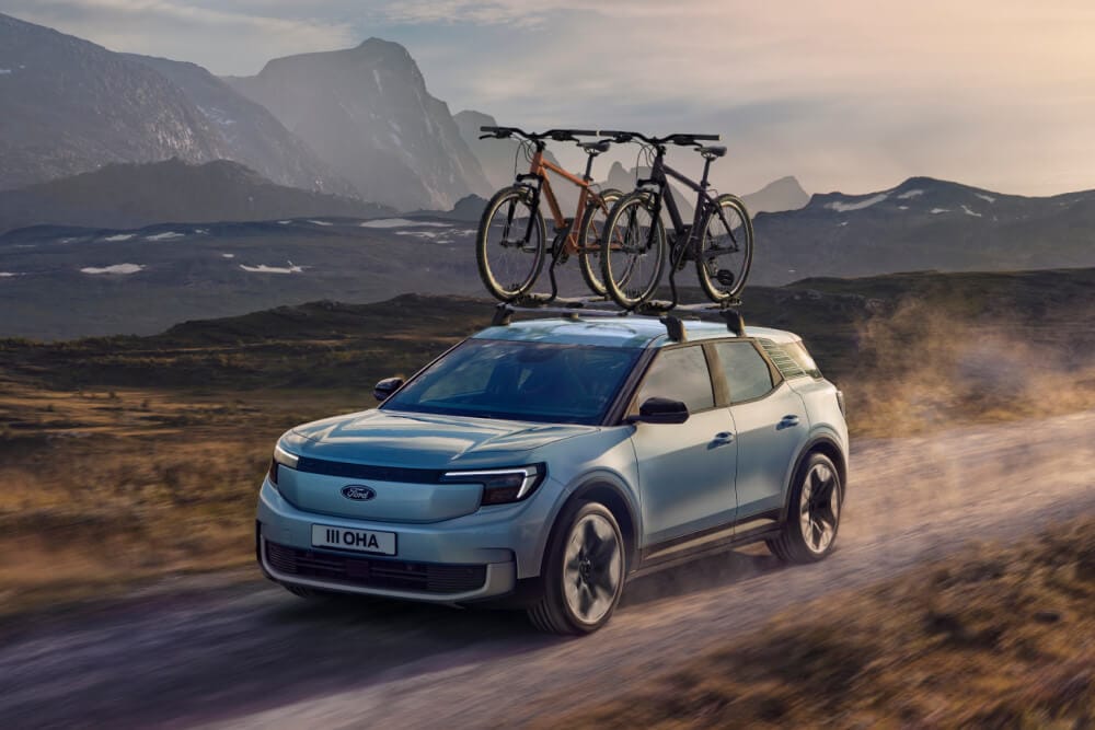 Blauer Ford Explorer auf einem unbefestigten Weg, mit Querträgern, einem Dach-Fahrradträger und zwei auf dem Dach montierten Fahrrädern.