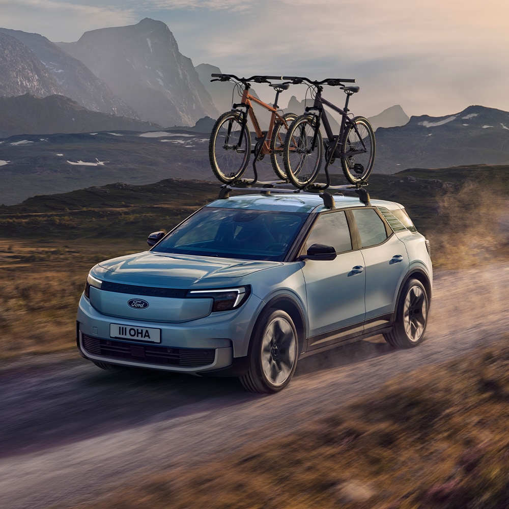 Blauer Ford Explorer auf einem unbefestigten Weg, mit Querträgern, einem Dach-Fahrradträger und zwei auf dem Dach montierten Fahrrädern.