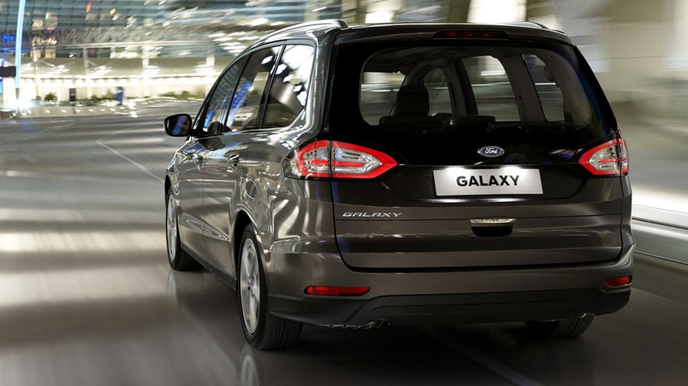 Ford Galaxy Hybrid in Schwarz. ¾-Heckansicht. Fahrszene bei Nacht durch eine Stadt