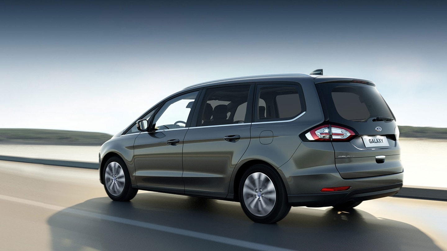 Ford Galaxy Hybrid in Grau, Dreiviertelansicht, bei Sonnenschein entlang einer Küstenstraße fahrend