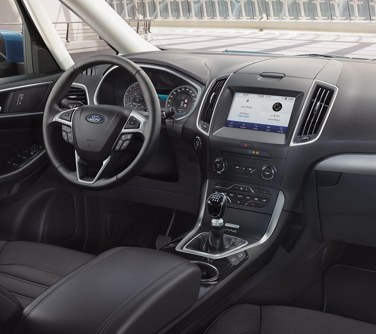 Ford Galaxy Hybrid in Grau, Dreiviertelansicht, bei Sonnenschein entlang einer Küstenstraße fahrend