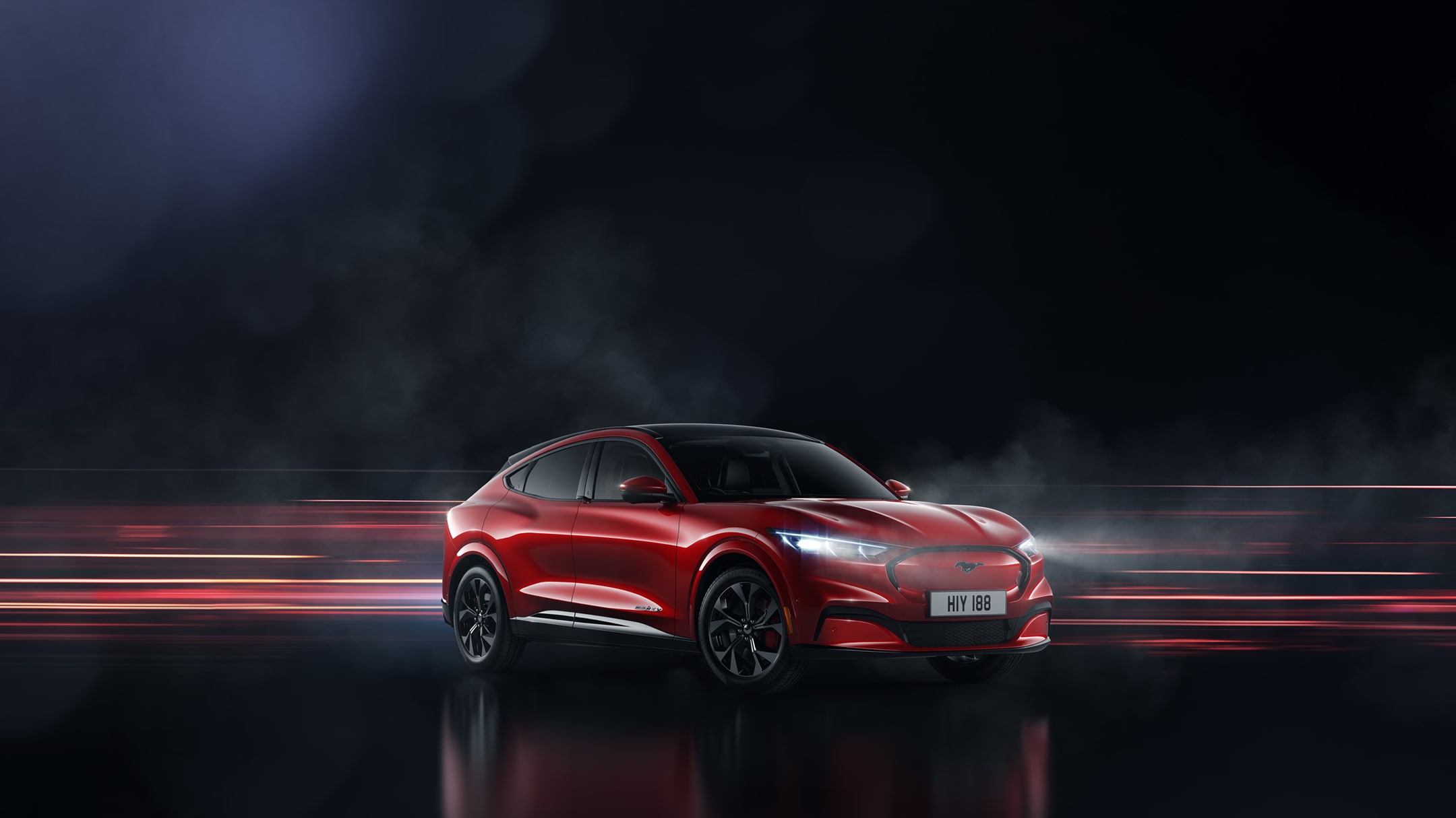 Ford Mustang Mach-E in Rot. Dreiviertelansicht, parkend vor dunklem Hintergrund