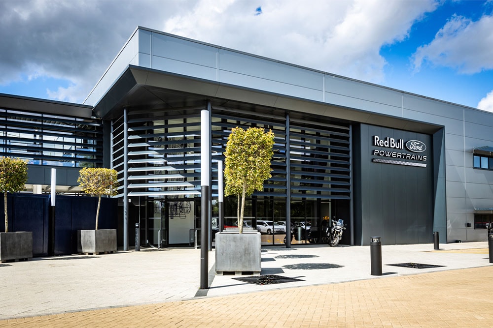 Das Hauptquartier von Red Bull Ford Powertrains – ein modernes Gebäude, an dessen Außenfassade das Firmenlogo angebracht ist.