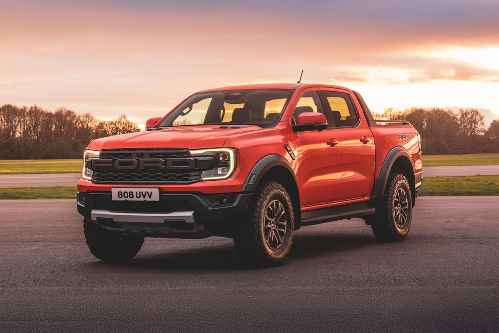 Ein orangefarbener Ford Ranger Raptor Pick-up-Truck, der in einer malerischen Landschaft geparkt ist.