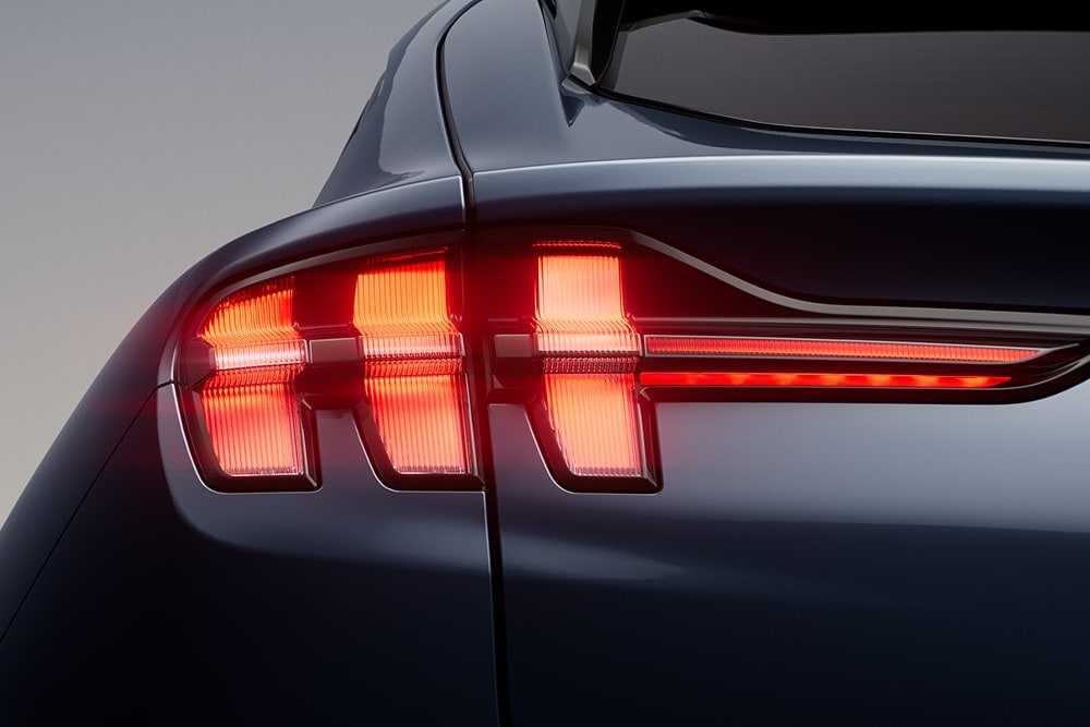Nahaufnahme der beleuchteten dreiteiligen Rückleuchten eines Ford Mustang Mach-E Sportwagens.