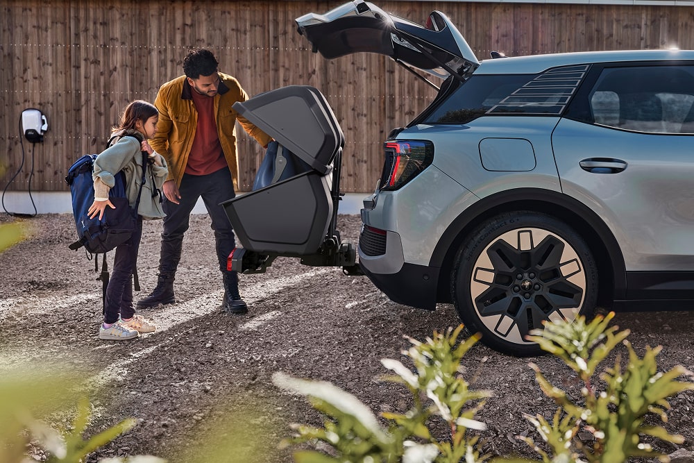 Ein Mann und ein Kind stehen neben dem offenen Kofferraum eines Ford Explorer SUV und laden einen zusammengeklappten Kinderwagen ein.