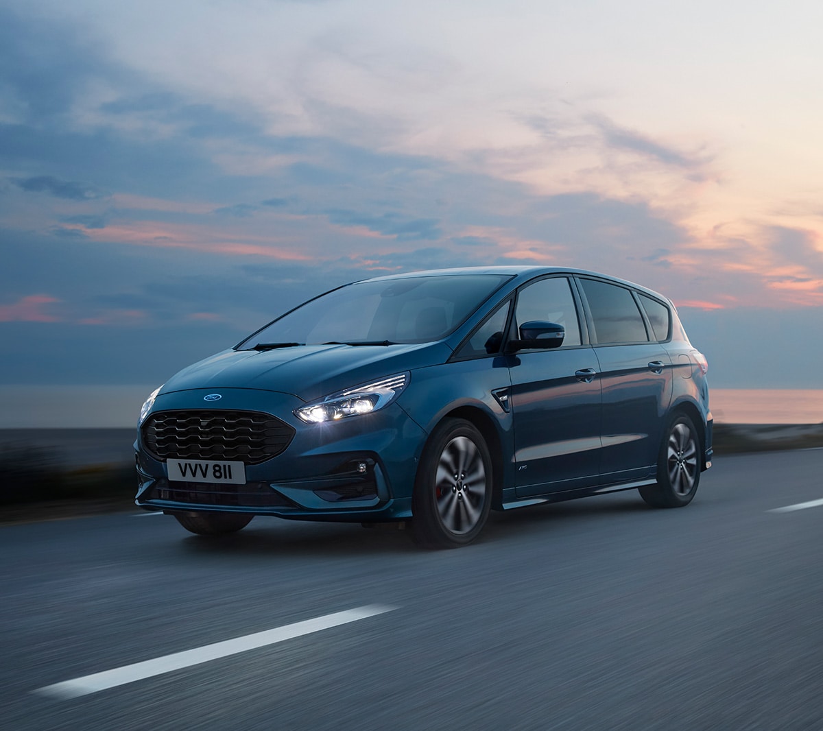 Ford S-MAX in Blau. ¾-Frontansicht. Fahrszende auf einer Küstenstraße bei Abenddämmerung