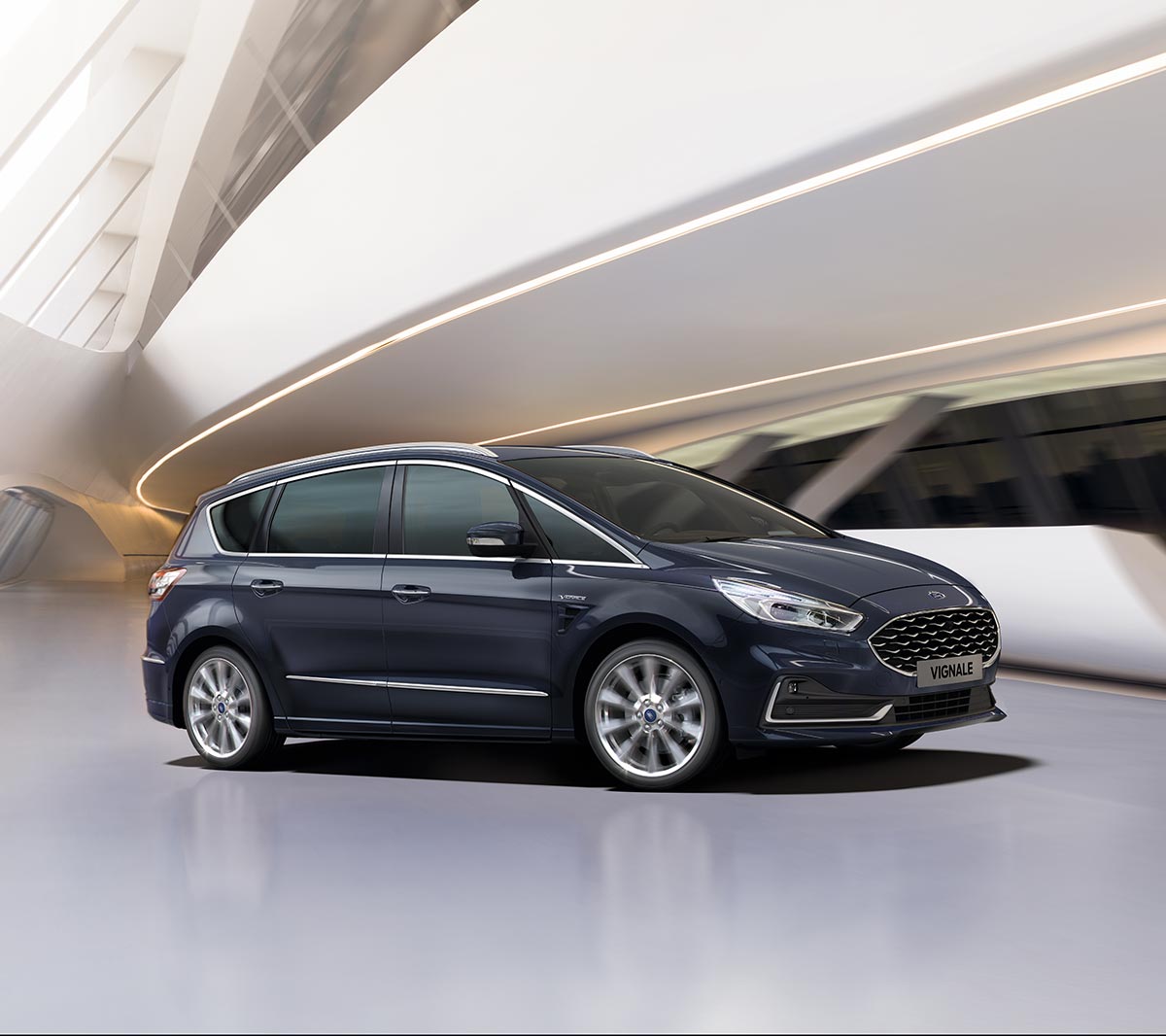 Ford S-MAX Hybrid in Blau. Dreiviertelansicht, fahrend vor futuristischem Gebäude
