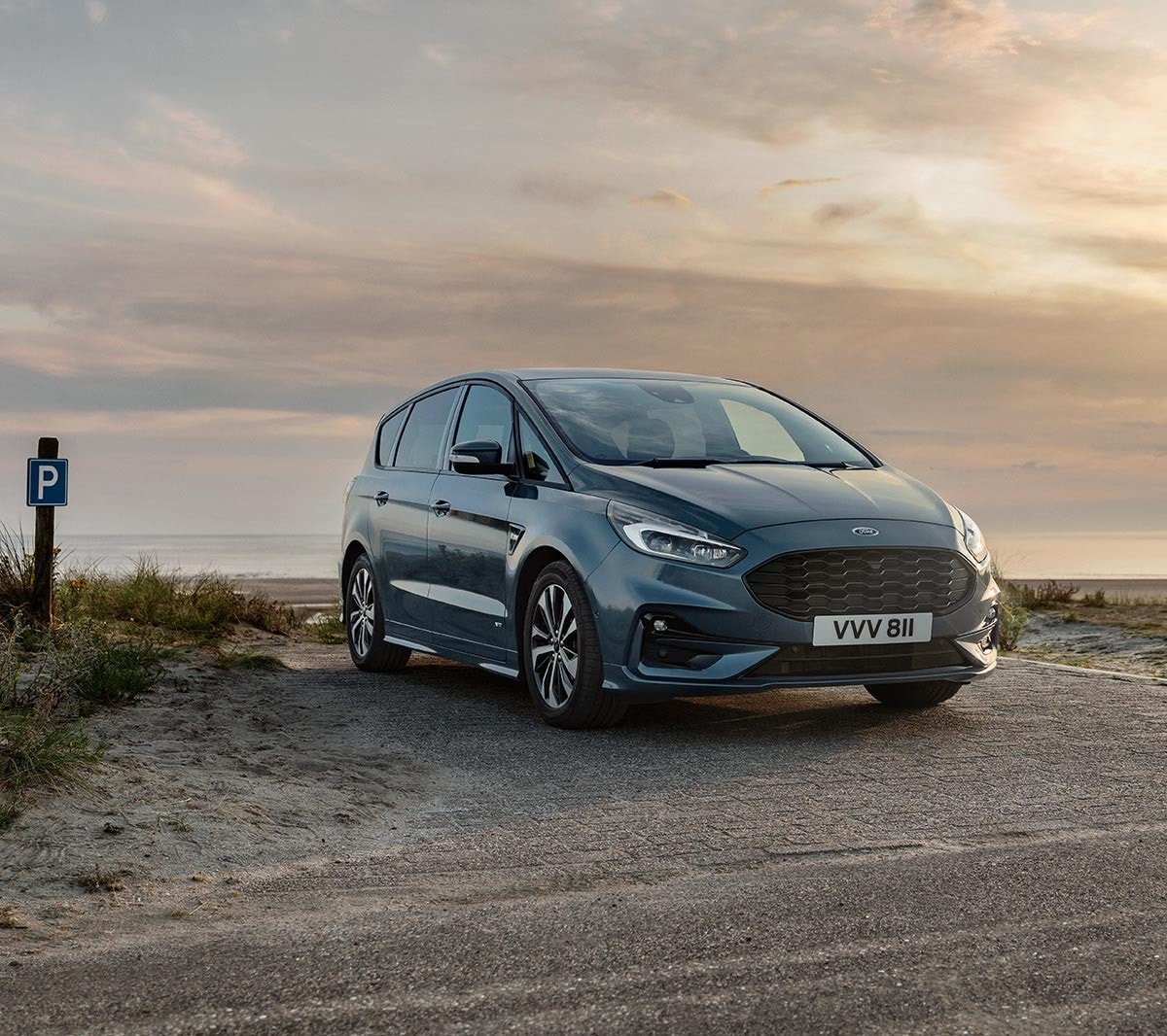 Ford S-MAX Hybrid in Blau. Dreiviertelansicht, parkend am Strand bei Sonnenuntergang