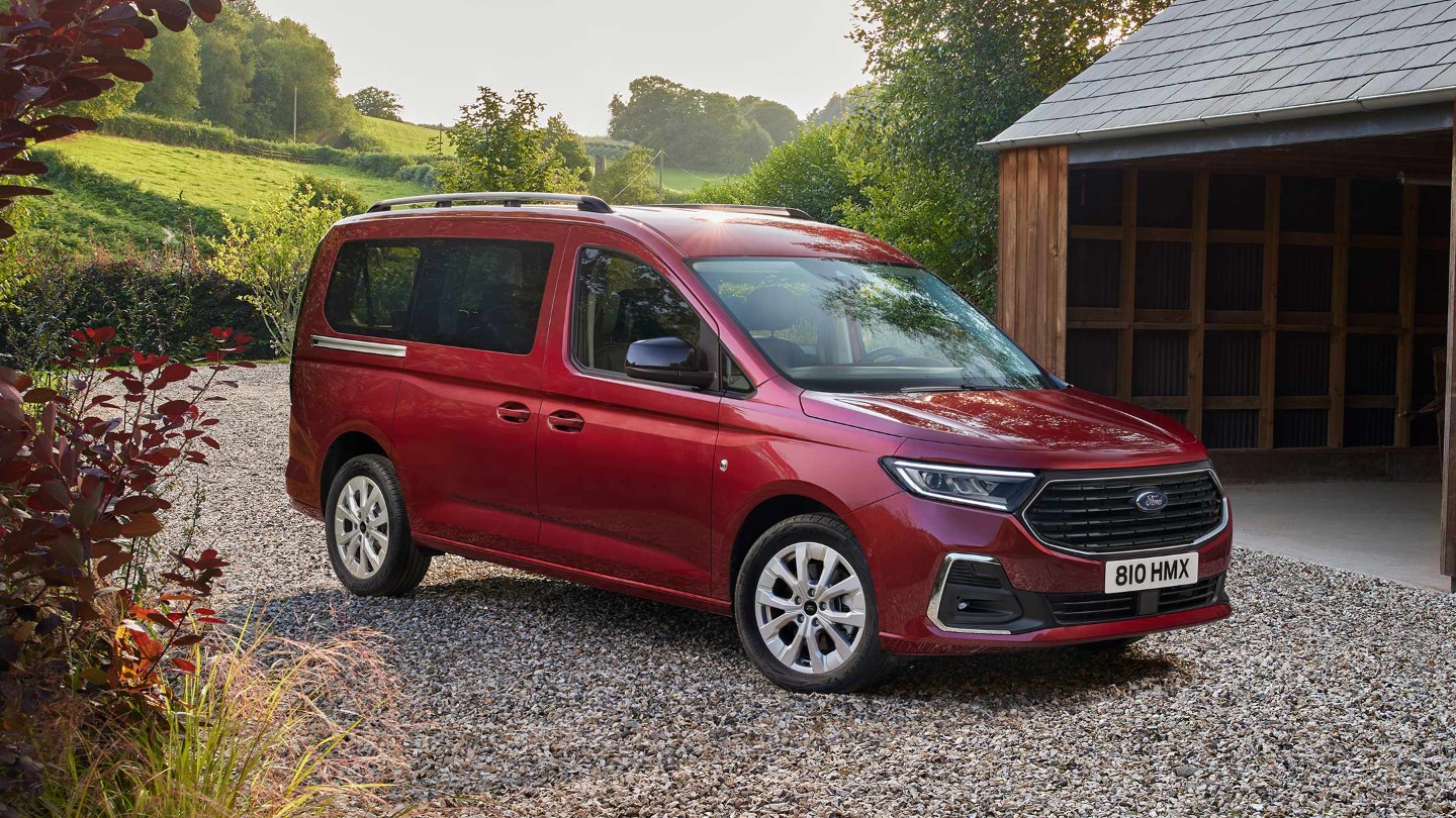 Ford Grand Tourneo Connect in Rot ¾-Frontansicht parkt auf Kiesweg vor Wohnhaus