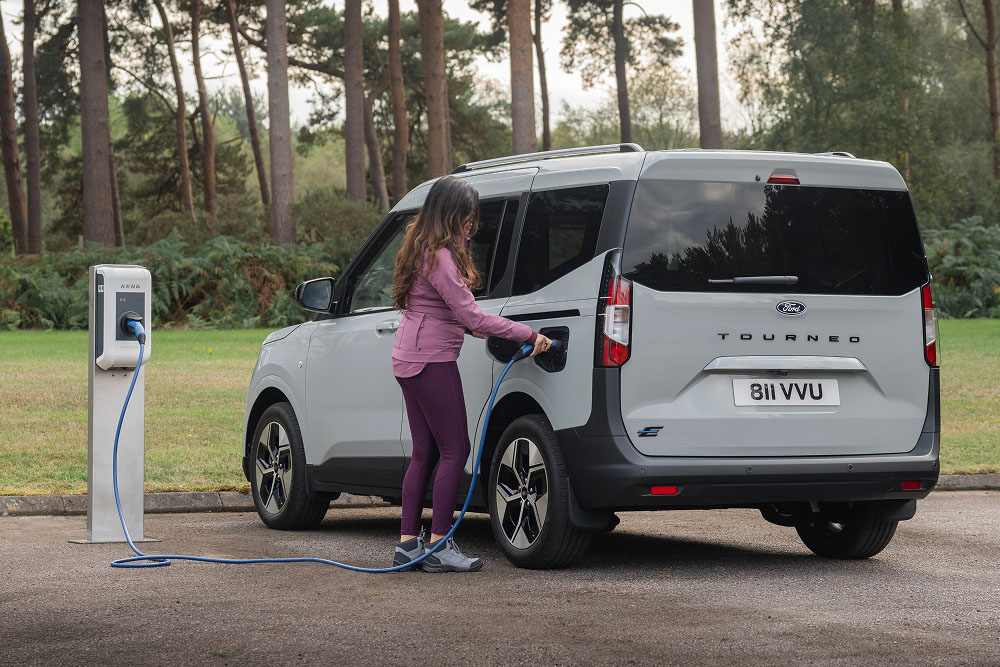 A person plugs a grey Ford E-Tourneo Courier into an outdoor charging station.