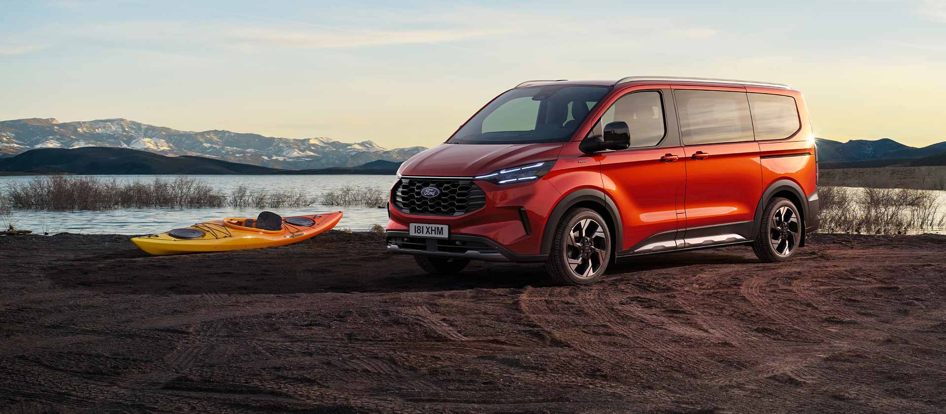Roter Ford Tourneo Custom Transporter parkt nahe einem See mit einem Kajak.