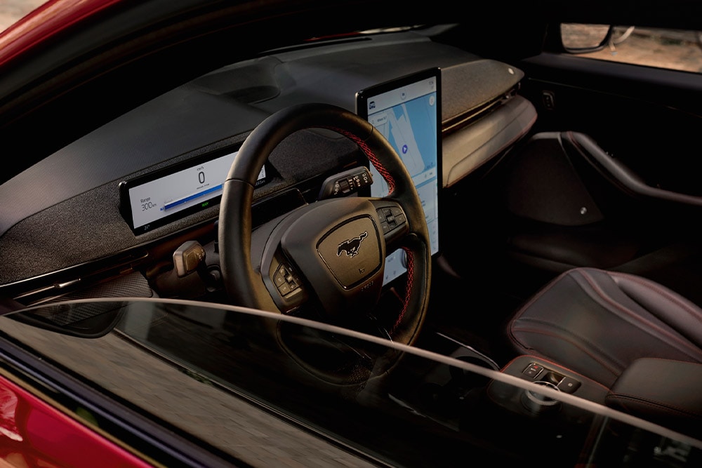 Innenansicht eines Ford Mustang Mach-E mit Lenkrad, digitalem Kombiinstrument und großem zentralen Touchscreen.