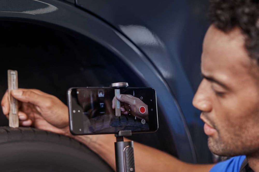 Ford-Techniker nimmt mit einem Smartphone ein Video bei der Kontrolle eines Fahrzeugreifens auf.