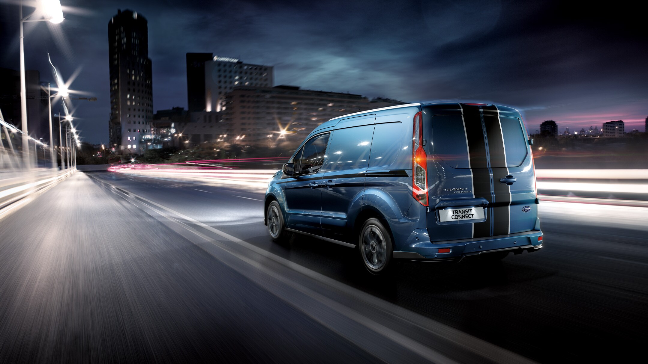 Ford Transit Connect in Blau ¾-Heckansicht fährt bei Nacht durch Großstadt 