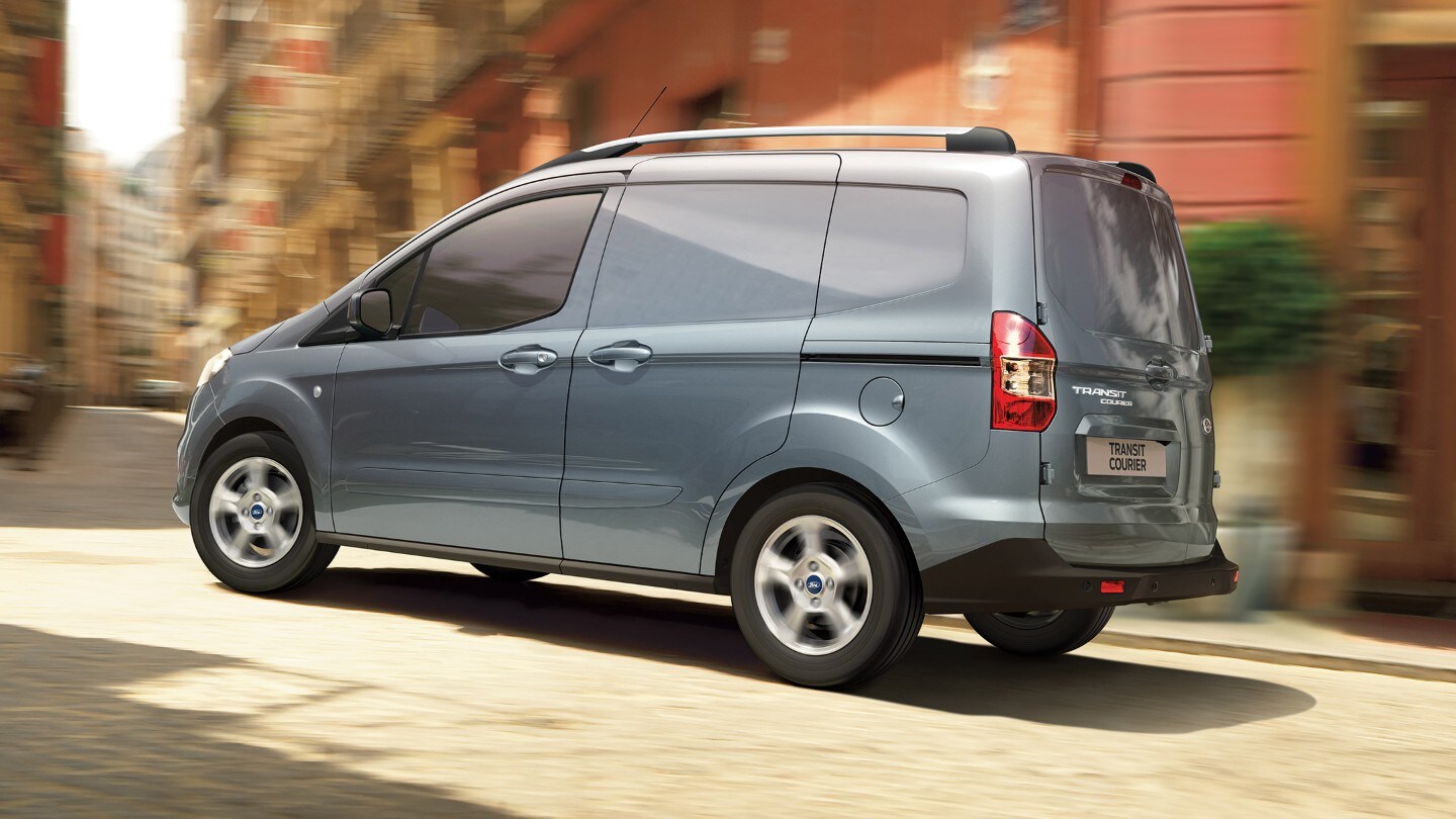 Ford Transit Courier in Grau Seitenansicht fährt durch enge Straßen in der Innenstadt