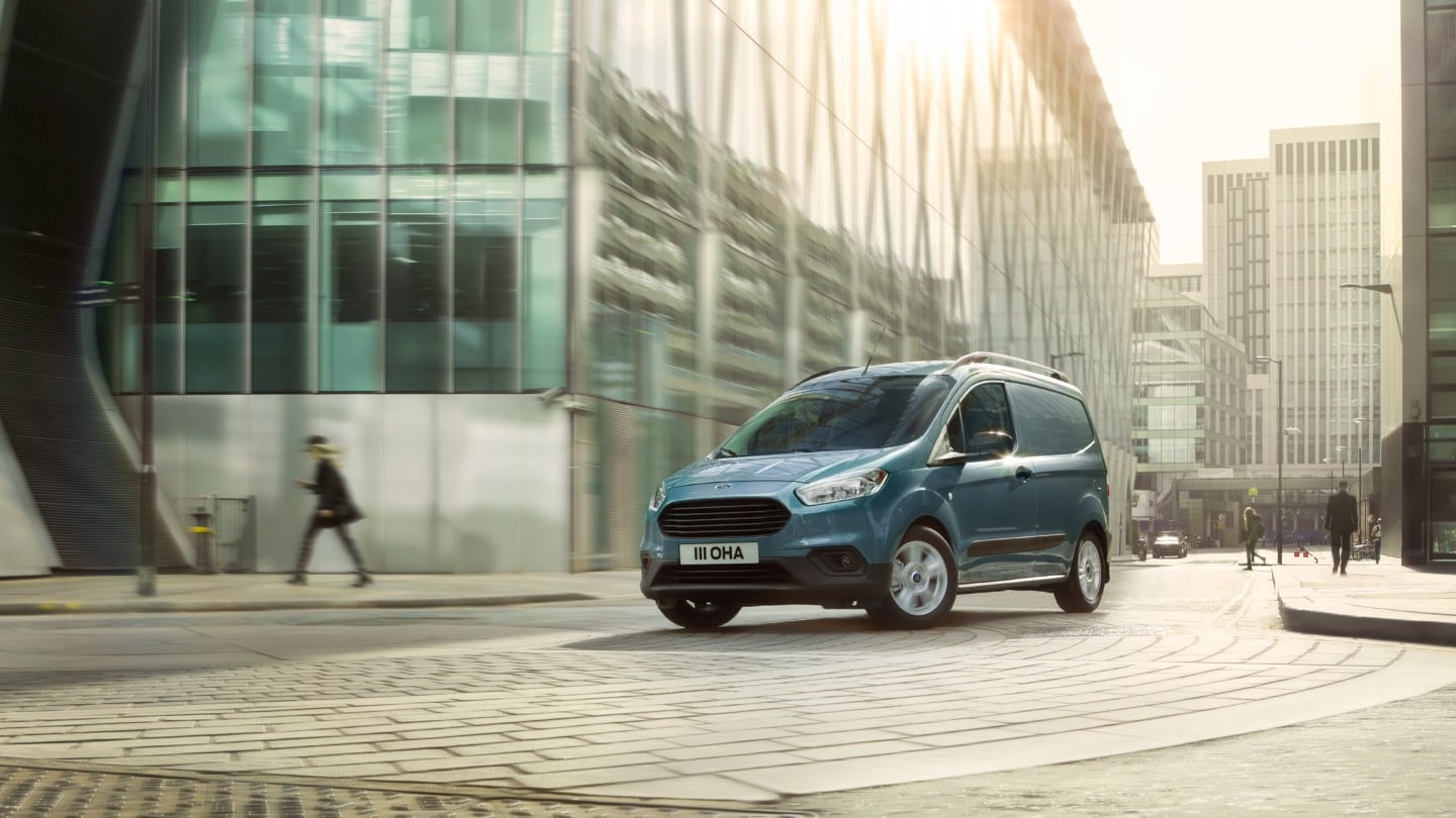 Ford Transit Courier in Grau ¾-Frontansicht fährt durch enge Straßen in der Innenstadt